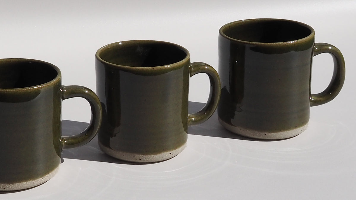 Three dark olive green ceramic mugs with a glossy finish and an unglazed stoneware base.