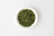 White bowl filled with Shiraore green tea leaves on a white background